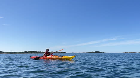 girl paddling on a bright orange kayak in open water with islands in the background on a sunny day