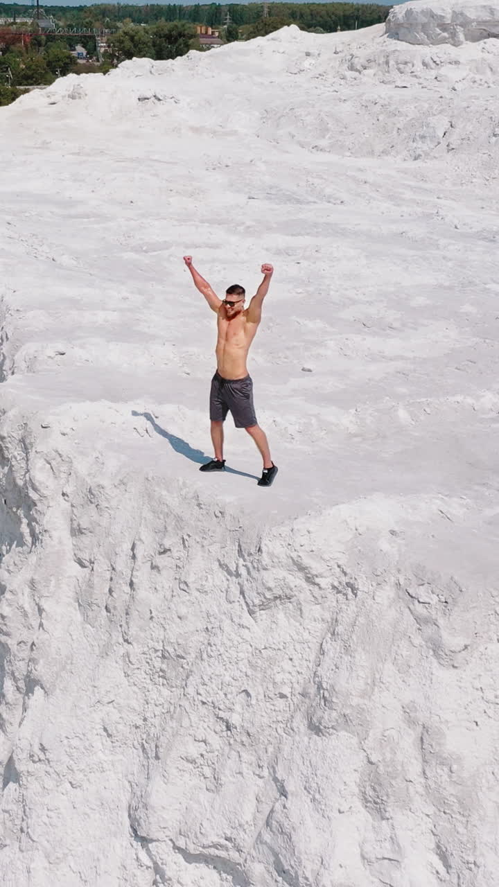 Happy sportsman on natural background. Muscular athlete raises his arms while standing on rocky hill in the countryside. Vertical video
