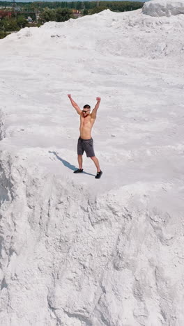 happy sportsman on natural background. muscular athlete raises his arms while standing on rocky hill in the countryside. vertical video