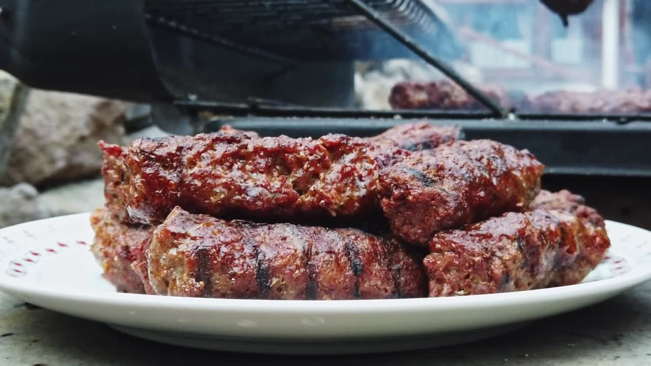 Man put grilled sausage on the plate using tongs. Slow motion. Close up