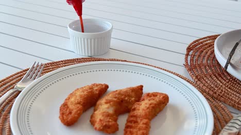 a sequence showing sauce being poured over golden fried chicken on a white plate, set on a woven placemat