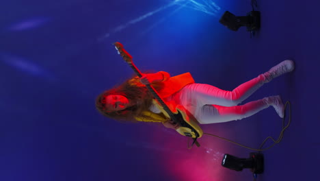 video vertical de una mujer loca tocando el bajo en un estudio bailando y mirando a la cámara y saltando sobre el fondo azul del estudio