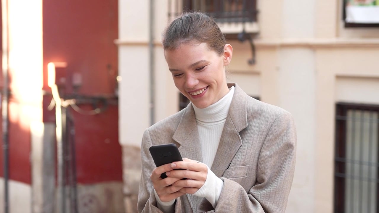 Una giovane donna è completamente assorta con il suo smartphone mentre si trova in un contesto urbano.