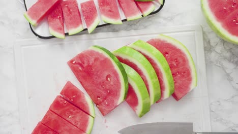 slicing red watermelon into small pieces on a white cutting board.