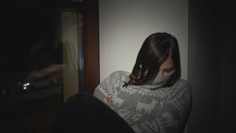 a young woman sits alone by a window at night