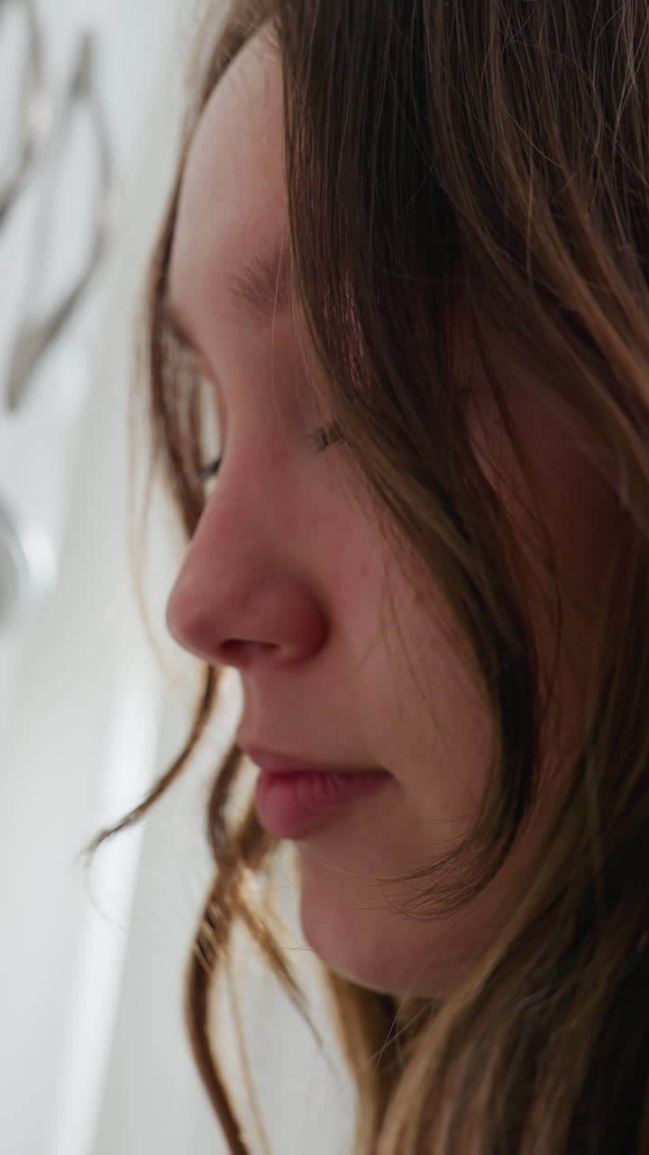 Close-up head view of elegant lady with long brown hair partially covering her face, soft natural lighting, serene expression, white kitchen cabinet background