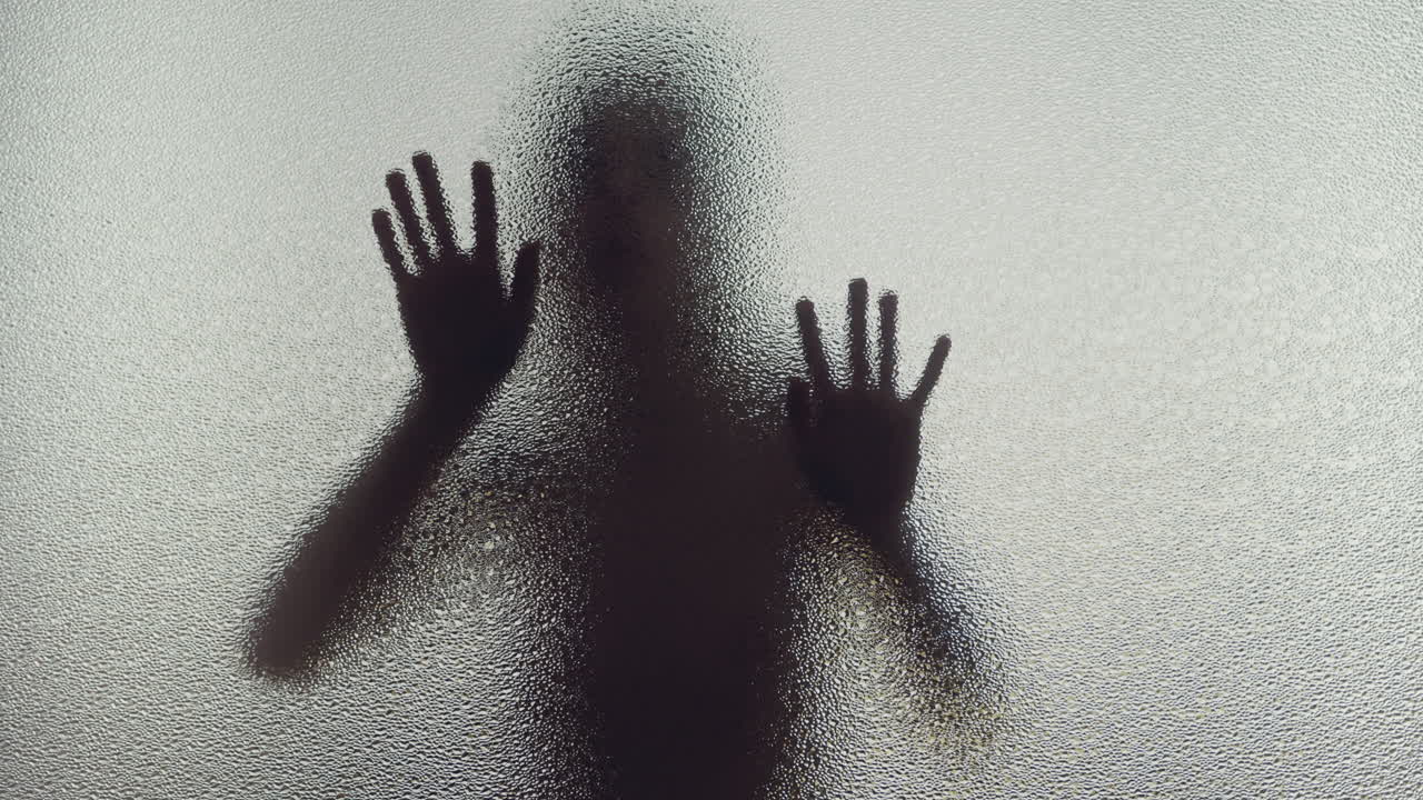 A female silhouette behind the frosted window slowly touches the glass