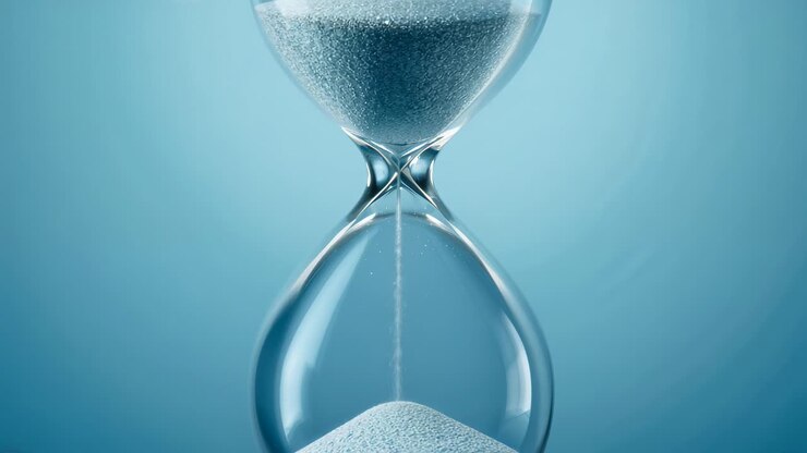 Frame capturing hourglass trickling fine white sand into lower bulb against light blue gradient