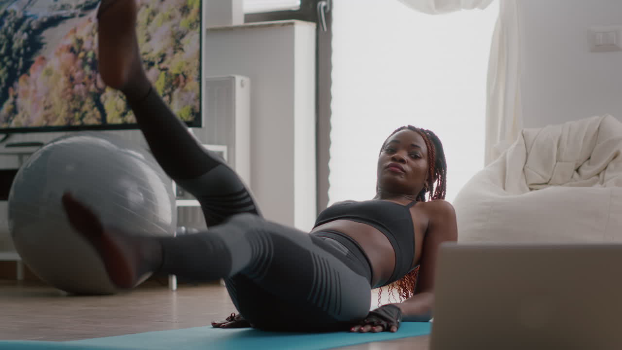 African slim woman morning workout in living room doing scissors exercise on yoga map