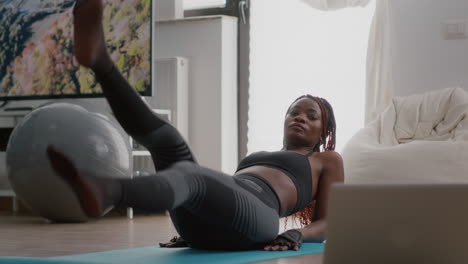african slim woman morning workout in living room doing scissors exercise on yoga map