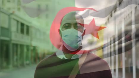 animation of flag of algeria waving over african american man wearing face mask in city street