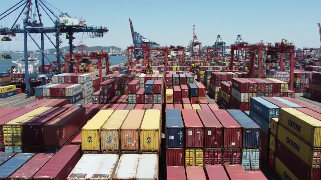 Stacks of colorful shipping containers fill a busy port, with cranes lifting cargo under a clear sky. The impressive activity highlights global trade in action.