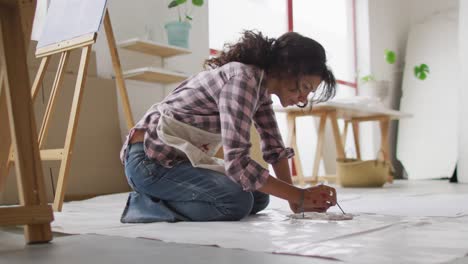 video of biracial female artist painting on floor in studio