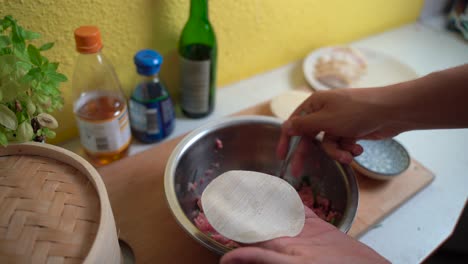 manos masculinas preparando albóndigas gyoza japonesas en una cocina luminosa con cuchara, vista bloqueada