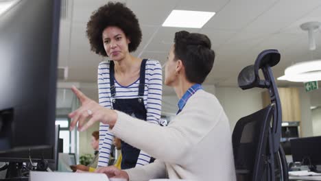 diversas compañeras de negocios sonrientes apuntando a la computadora y discutiendo en la oficina
