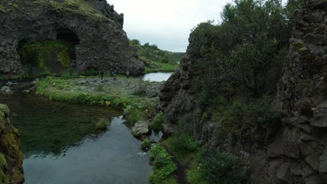 Flying-through-cave-at-Gjain-waterfalls,-scenic-cascade-in-Iceland,-cloudy-day