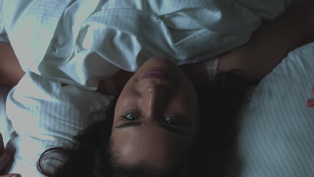 Morning wake up. The young woman woke up after a night in bed. She stretches while lying down and smiles at the camera. Rest in the bedroom