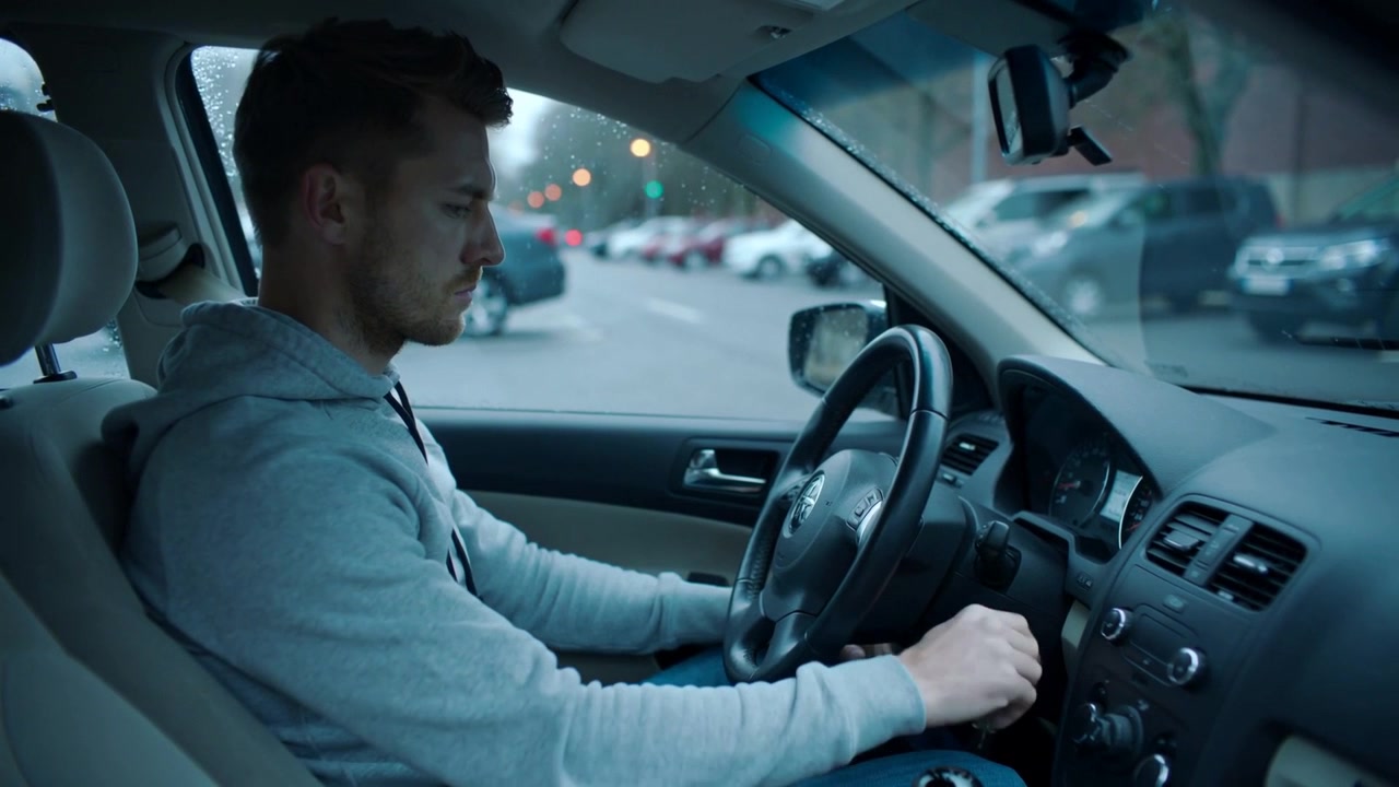 Turning man in light-gray hoodie and jeans turning car key, adjusting dash knob, preparing to drive