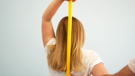 blonde woman doing shoulder mobility exercise with stick supervised by physiotherapist