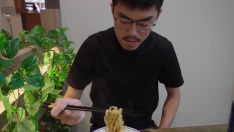 hombre comiendo sopa tradicional asiática de fideos singapurenses en cámara lenta meepok con huevo y carne picada