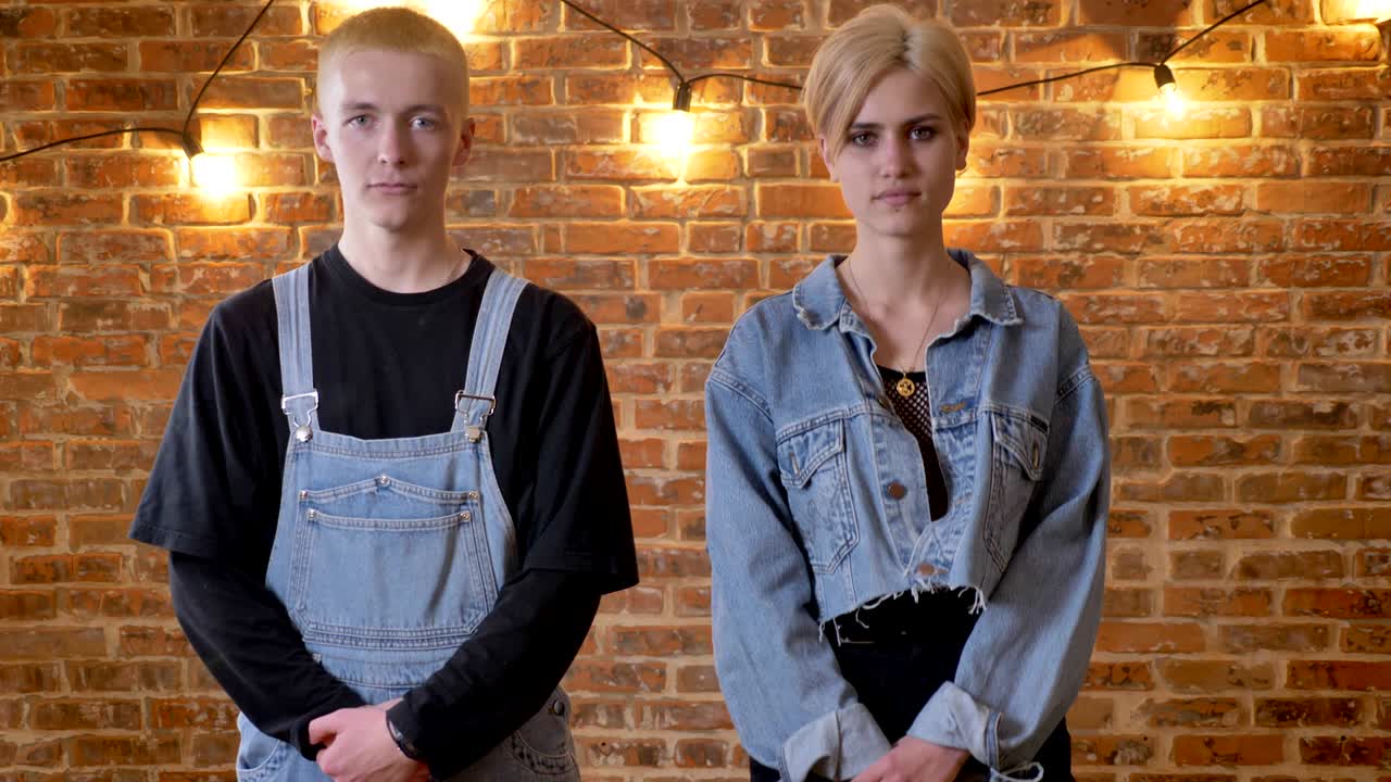 Young couple of hipsters is dancing, jumping, squating, fooling around, move conception, brick background