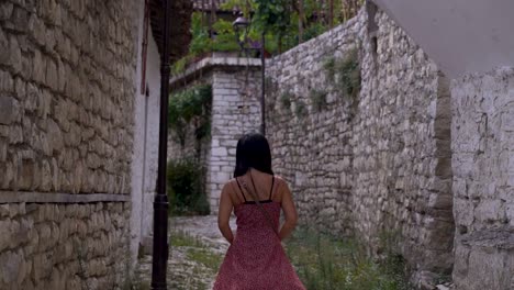 Chica-Vestida-De-Verano-Caminando-Por-Un-Callejón-Estrecho-Con-Edificios-De-Piedra