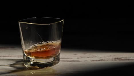Person-filling-transparent-glass-with-bourbon-on-wooden-table-in-rays-against-black-background