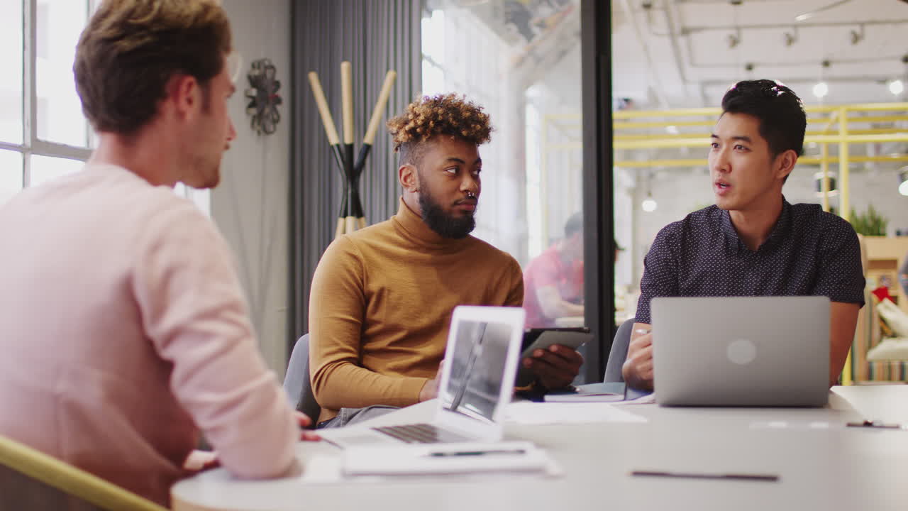 Young male creative business team discussing a project in a meeting room, close up, low angle