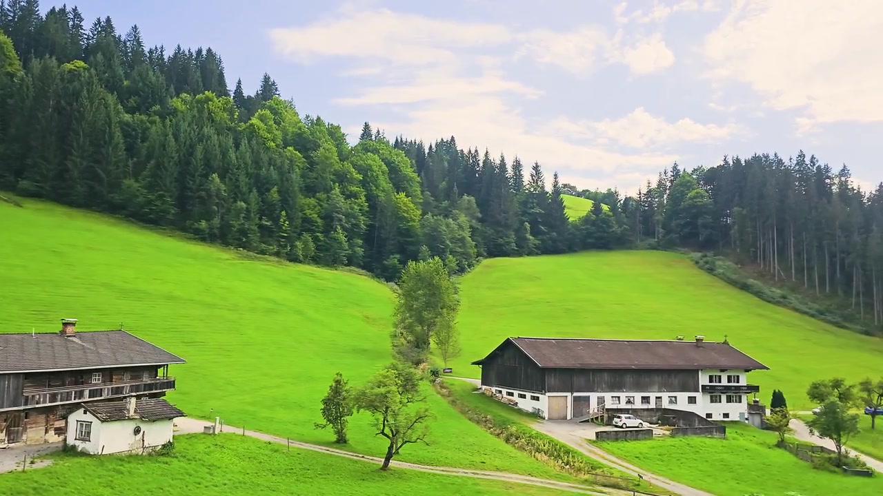 Panorama dal finestrino del treno in Austria con campi verdi vividi, edifici rurali, pendii boscosi e montagne alpine blu, ideale per contenuti di turismo e viaggio
