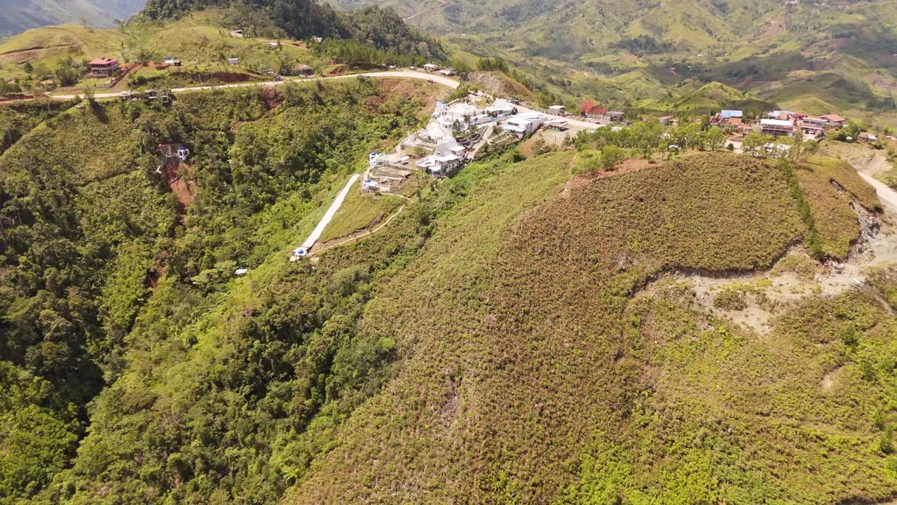 4K aerial drone shot of lush mountain slopes, hillside structures, and rural roads in the Philippines under bright daylight, revealing dense green vegetation and tropical highland terrain