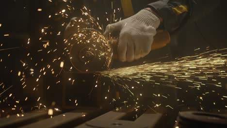 industrial worker using an angle grinder and cutting a metal square pipe. locksmith in special clothes in production. industry machinery plant interior. manufacturing metal structures. close up, 4k