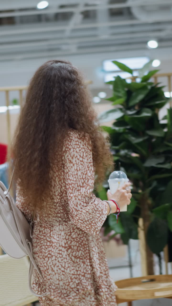 Woman with backpack walks through brightly lit clothing store, browsing various outfits on display with other shoppers around, her focused expression captures her exploration of modern fashion