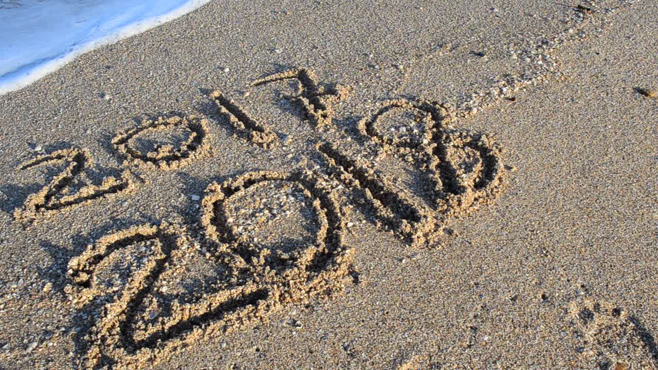 Iscrizione 2017 e 2018 sulla sabbia. Iscrizione 2017 e 2018 sulla sabbia. L'iscrizione 2017 viene cancellata da un'onda marina