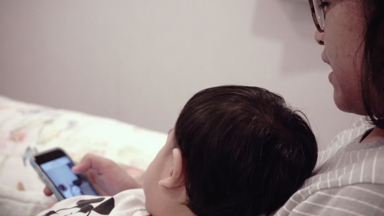 침대에 있는 엄마와 함께 드폰을 사용하는 아시아 아기