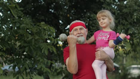 Granddaughter-and-grandfather-doing-fitness-exercises-with-dumbbells.-Senior-man-with-child-kid-girl