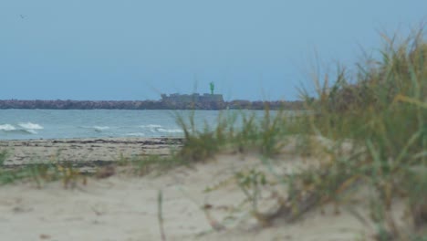 Vista-Distante-En-ángulo-Bajo-Del-Muelle-De-Piedra-Cerca-Del-Puerto-De-Liepaja-,-Día-De-Otoño-Nublado,-Playa-De-Arena-Blanca-En-Primer-Plano,-Mar-Tranquilo