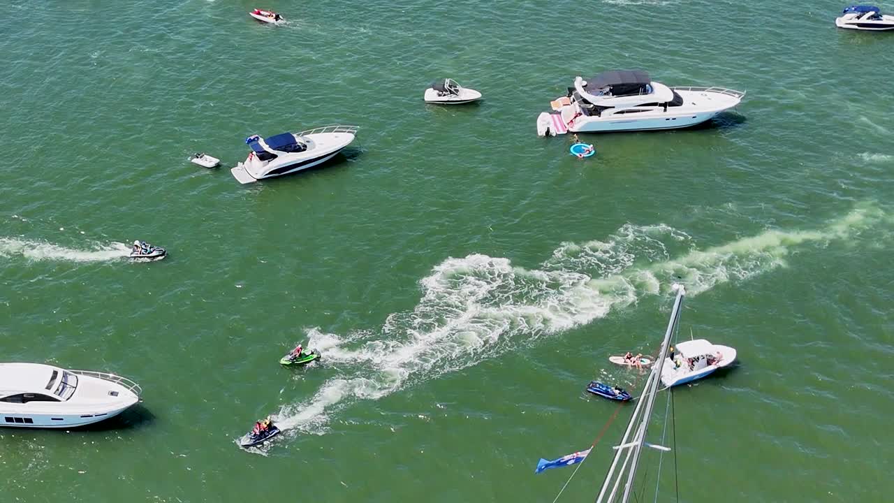 Aerial view of boats and jet skis creating dynamic patterns on green waters.