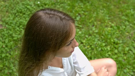 portrait of a beautiful young woman in a white dress sits on the grass in the garden on a warm summer day and smiles at the camera