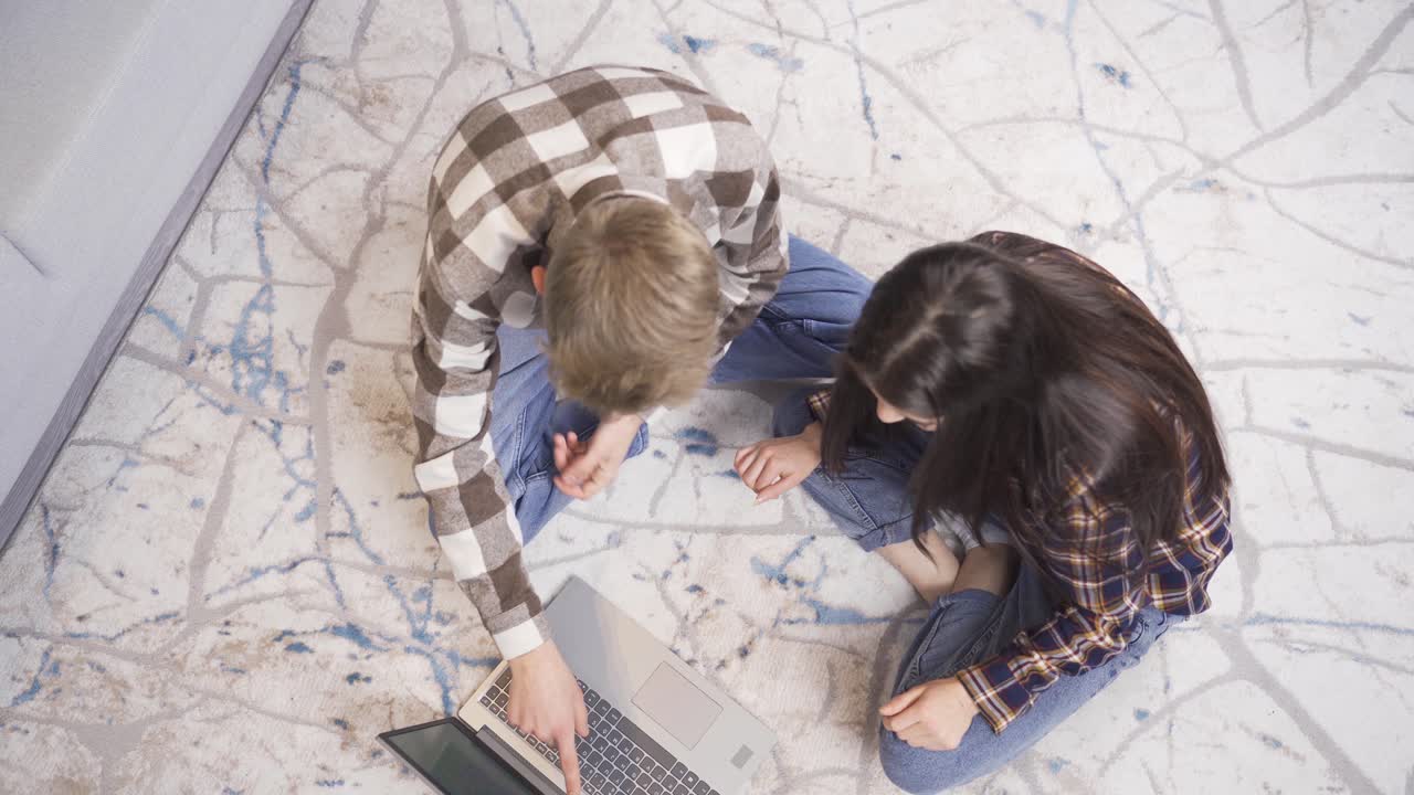 положительный счастливый молодой мужчина и женщина смотрят на ноутбук дома и улыбаются.