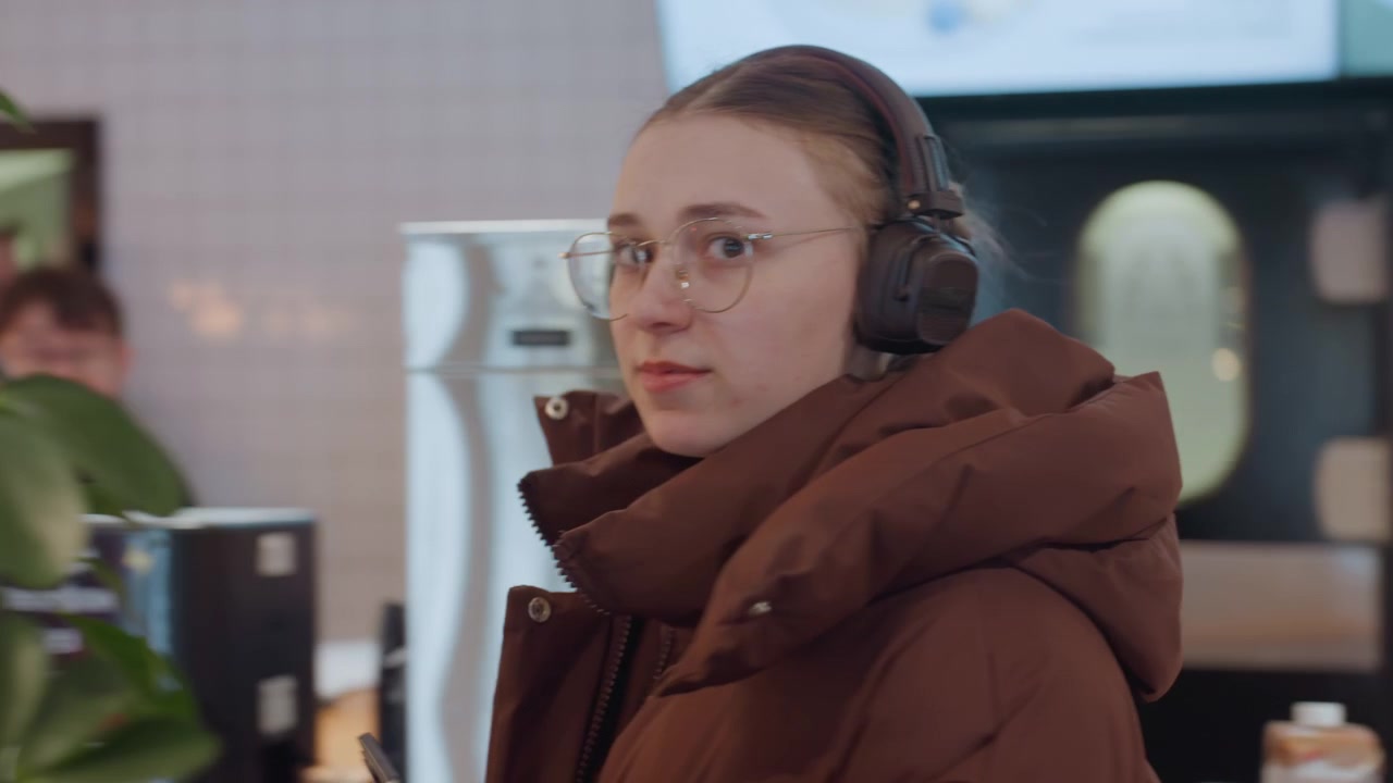 Mladá žena se sluchátky používající telefon v moderní kavárně