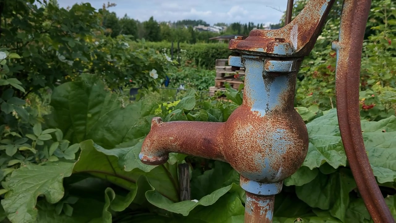 Pompa a mano vintage arrugginita in giardino, dettaglio di giardinaggio in primo piano