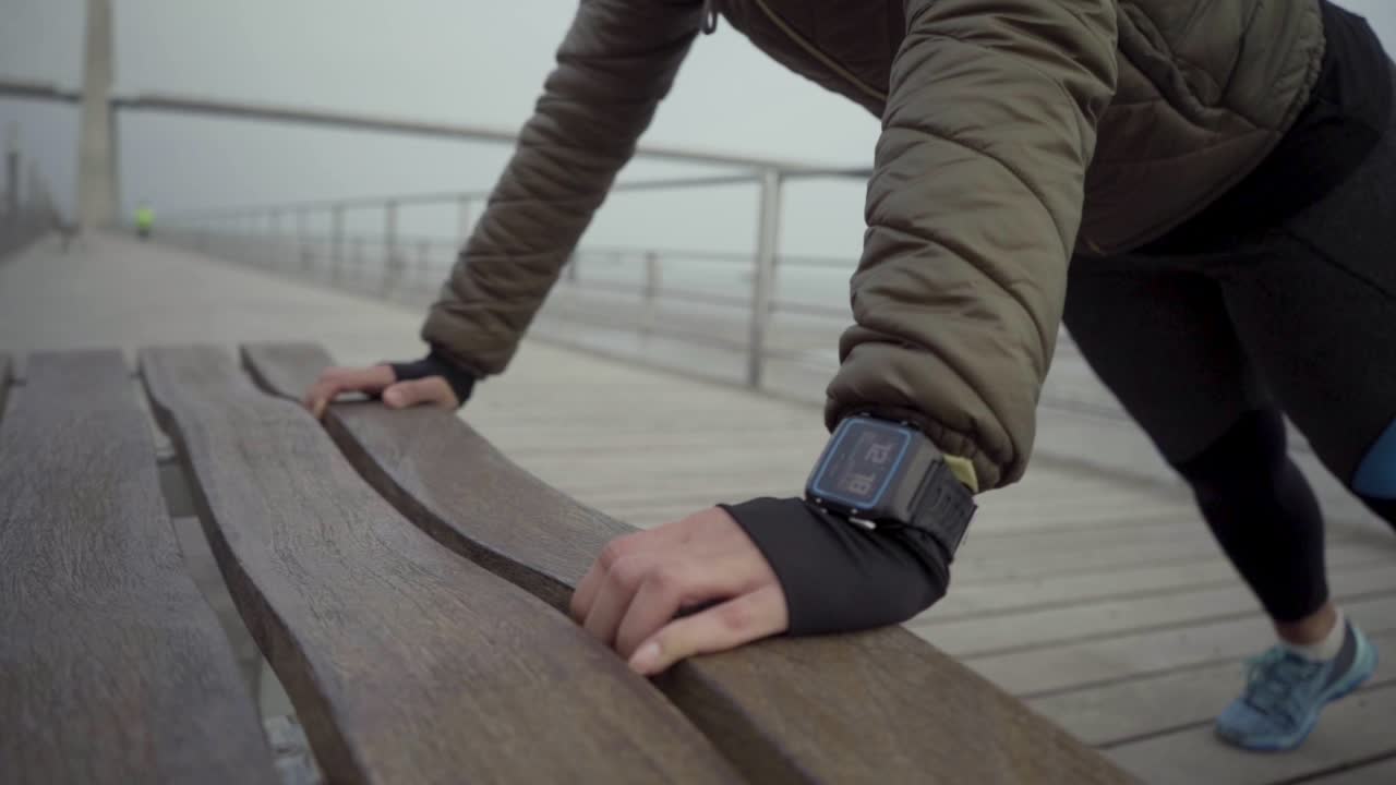 갈색 젊은 여성은 바 ⁇ 에서 나무 벤치에서 심각한 푸시 업을하고 있습니다.