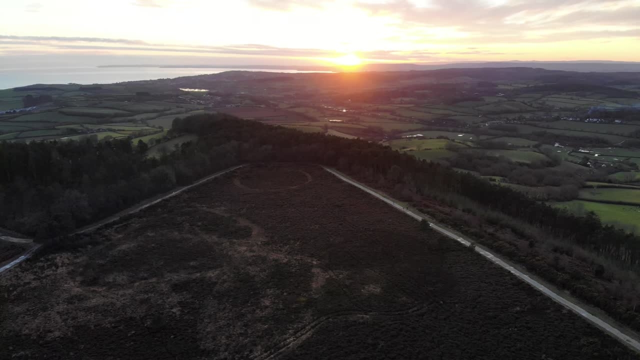 Sunset illuminating Mutters Moor and the surrounding countryside near Sidmouth, East Devon, aerial view at golden hour. circle dolly