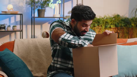 happy indian man shopper unpacking cardboard box delivery parcel online shopping purchase at home