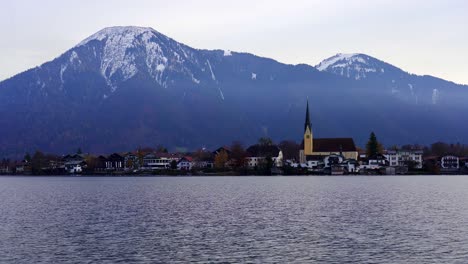 background view of stunning snow capped mountains with a church across the waters of tegernsee