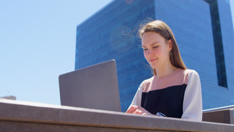 Front-view-of-young-cool-caucasian-businesswoman-working-on-laptop-in-balcony-of-modern-office-4k