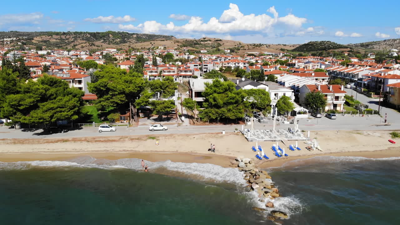 Aerial drone view of the Aegean sea coast in Nikiti, Greece. Beach with terraces, umbrellas and sunbeds on embankment street, multiple buildings