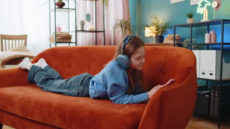 feliz niña caucásica niño en auriculares inalámbricos relajándose acostado en el sofá en casa escuchando música