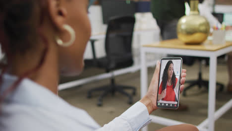 mujer de negocios afroamericana que usa un teléfono inteligente para una videollamada con un colega de negocios biracial