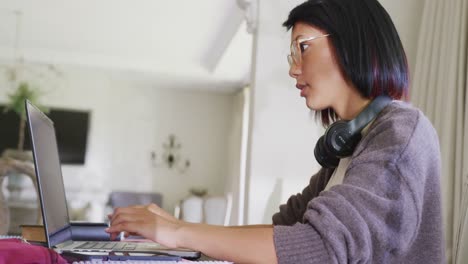 happy biracial teenager girl sitting at table and using laptop, in slow motion